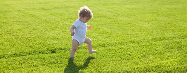 Banner con cara de niño primaveral. Banner con cara de niño primaveral. Primer paso. Bebé piernas desnudas de pie sobre hierba verde. Una niña sana. Niños sobre hierba verde fondo. —  Fotos de Stock