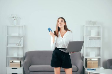 Dizüstü bilgisayarı ve kredi kartı olan genç bir iş kadını ofiste çok fazla işi olan bir bilgisayarla çalışıyor. Sekreter kız.