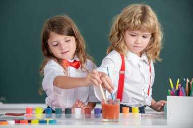 Sınıfta karatahta arka planda komik öğrenciler çiziyor. Okul arkadaşları çocuklar, kız ve erkek birlikte resim yapıyorlar. Çocukluk eğitimi, çocukların sanatsal becerileri..