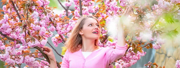 Coppia primaverile innamorata, striscione. Donna bionda godendo un momento in fioritura giardino sakura. Giorno soleggiato di primavera. Ragazza felice trascorrere del tempo in primavera fioritura albero giardino. — Foto Stock
