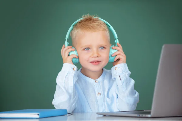 Garçon intelligent de l'école, élève mignon porte des écouteurs écrit sur ordinateur portable, écouter leçon audio utiliser ordinateur. Formation informatique. — Photo