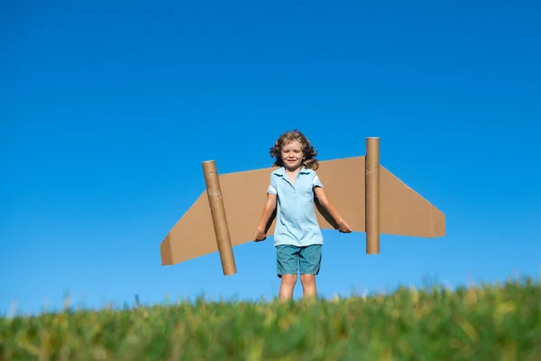 おもちゃのジェットパック屋外の子供。段ボールの翼を持つ緑の春のフィールドで遊ぶ子供。春の旅行と冒険. — ストック写真