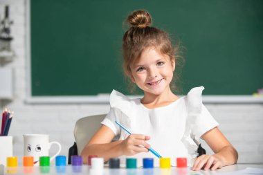 Okulda gülümseyen sevimli anaokulu çocuğu kız çizimi. İlkokulda resim yapan kız çocuğu. Erken eğitim.