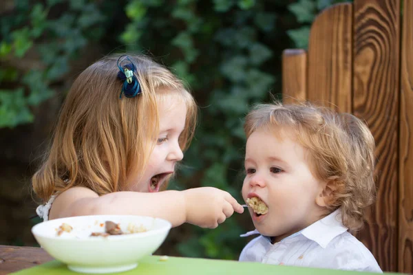 Baby kind eet voedsel. Klein meisje zus voedt baby. — Stockfoto
