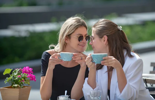 Dos jóvenes hablan y beben café en la cafetería, al aire libre. Mujeres jóvenes con tazas de café en el café. Vacaciones en Europa. —  Fotos de Stock
