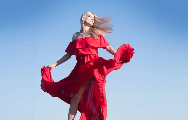 Femme blonde en robe rouge mouvement sur le ciel. Jeune modèle à la mode en robe de style. Femme de mode en été. — Photo