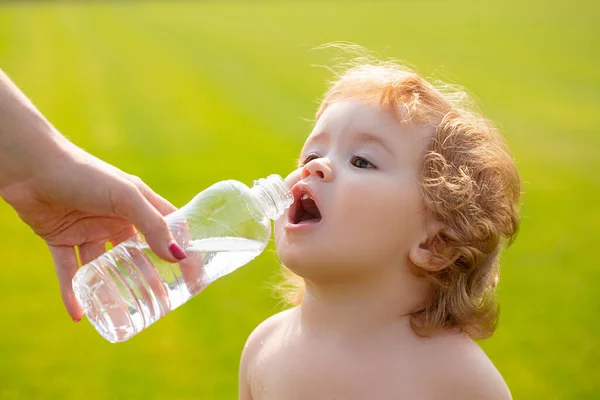 Ребенок пьет воду из рук матери. Ребенок пьет воду из бутылки во время прогулки по травяному полю, детское здоровье. Мать дает ребенку бутылку воды. — стоковое фото