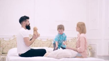 Anne baba ve çocuk yatakta oynuyorlar. Genç bir aile evde oyun oynuyor. Mutlu ebeveynler oğullarıyla yatakta oynuyorlar..