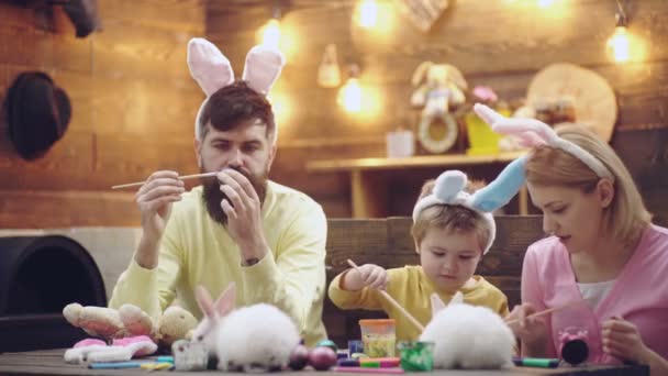 Familia de Pascua de madre, padre e hijo hijo pintaron huevos, usando orejas de conejo en el día de Pascua. Familia Celebrando la Pascua con los niños en casa. Vacaciones familiares de primavera. — Vídeos de Stock