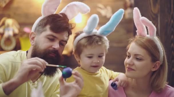 Szczęśliwa rodzina matki, ojca i syna malowała wielkanocne jajka, nosząc królicze uszy w Wielkanoc. Rodzinny wypoczynek. Zbliżenie twarzy. — Wideo stockowe
