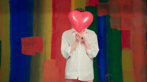 Mujer con globo de aire envía un beso de aire sobre fondo colorido. Una chica encantadora sostiene un globo. Mujer sorprendida sosteniendo globo en el estudio. — Vídeos de Stock