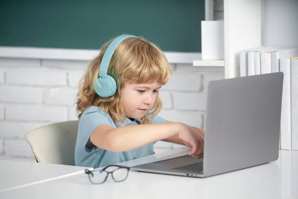 Niño pequeño en los auriculares ver video lección en la computadora en la escuela, niño en los auriculares tienen lección en línea, utilizando el ordenador portátil. Programación infantil Genius. — Foto de Stock