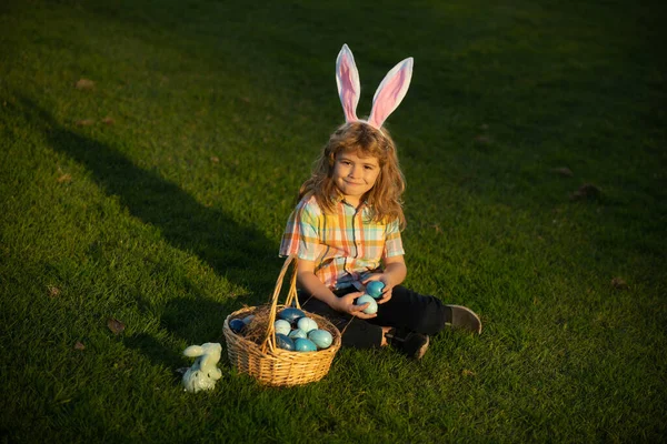 Enfant lapin mignon avec des oreilles de lapin. Enfant garçon chasse oeufs de Pâques dans la pelouse de printemps ponte sur l'herbe. — Photo