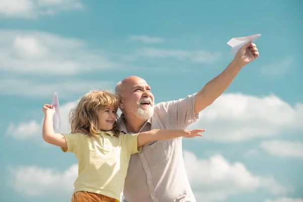 Child boy and grandfather with toy paper plane against summer sky background. Boy with dreams of flying. — Fotografia de Stock