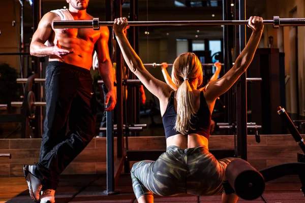 Entrenamiento de mujer fuerte con barra en el gimnasio. Entrenador muscular hombre mujer de entrenamiento con barra. — Foto de Stock