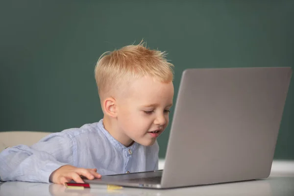 Kleine student die laptop computer gebruikt in de klas. Grappige blonde pupil op schoolbord. — Stockfoto