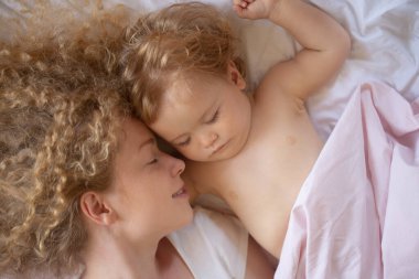 Anne ve bebek yatakta uyuyor. Sessiz bir uyku. Yatma zamanı, çocukluk ve aile konsepti, kapalı mekan portresi.