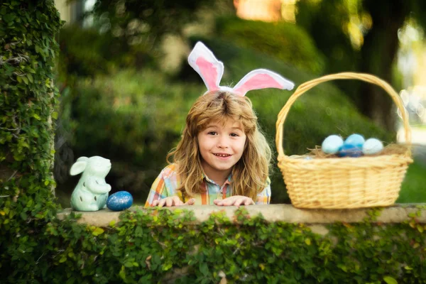 Portret van konijnenjongen op Paasdag. Kind jongen jagen eieren in de tuin, lente familie vakantie. Paashaas kinderen jagen op paaseieren met paasmand. Grappig kind gezicht dragen konijnenoren. — Stockfoto