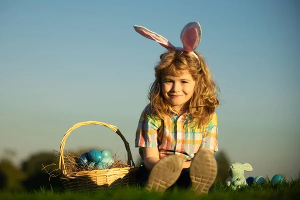Cute bunny child boy with rabbit ears. Children hunting easter eggs on sky background with copy space. Child with easter eggs and bunny ears, outdoor portrait. — Zdjęcie stockowe