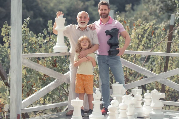 兴奋的爷爷和儿子下棋.不同年龄段的人玩棋盘游戏都很吃惊。三代男人. — 图库照片