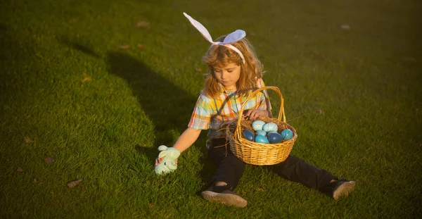 Roztomilý králíček s králičíma ušima. Děti loví velikonoční vajíčka na dvorku na zelené trávě. — Stock fotografie