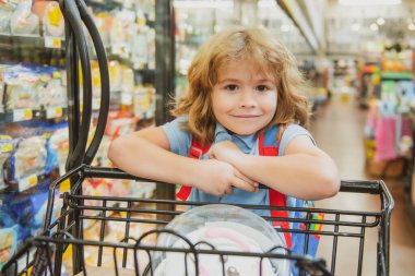 Marketten alışveriş sepeti alan bir çocuk. Müşteri ailesi süpermarketten ürün alıyor.