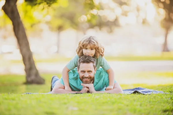Papá con niño lindo acostado en la hierba en el parque de verano al aire libre. Padre e hijo relajándose en la naturaleza. — Foto de Stock