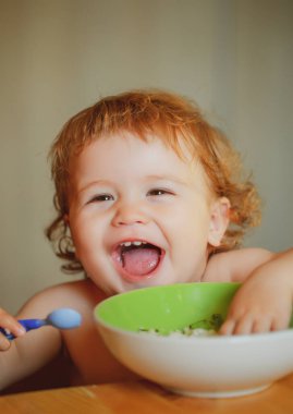 Gülümseyen bebek yemek yiyor. Cutr 'ın bebeği kaşıkla kendini yiyor. Çocuk yemek yiyor..