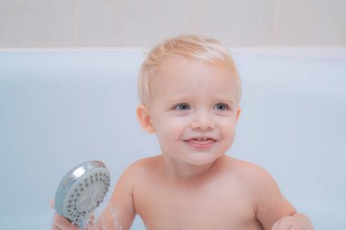 Komik şirin bebek banyo köpüğü içinde yüzüyor. Tatlı küçük bebek çocuk alarak banyo beyaz bir güneşli banyo köpük ve ördek oyuncaklar ile oynama.