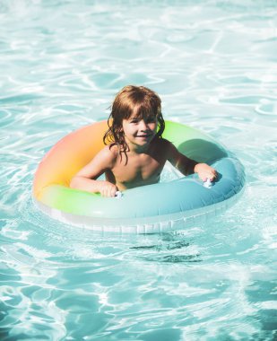 Mutlu çocuk yüzme havuzunda renkli yüzme yüzüğüyle oynuyor. Çocuk oyuncakları. Çocuklar tropikal tatil köylerinde oynarlar. Aile plaj tatili ve yaz etkinliği.