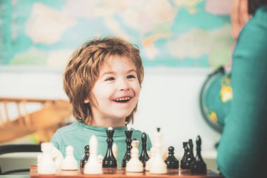 Küçük çocuk satranç oynuyor ve eğleniyor. Neşeli gülümseyen küçük çocuk masada oturuyor ve akşam keyfi ile satranç oynuyor..