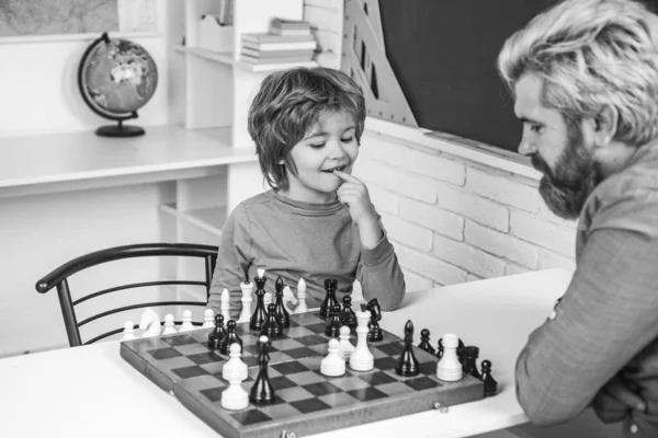 Cute little boy playing chess with father. Handsome teacher giving private lessons chess to preschool boy. Back to school. Happy Father and son.