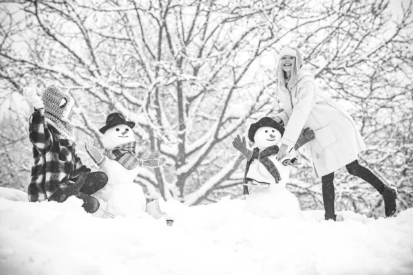 Przyjaciółki Hipster Girls bawią się ze Snowmanem na śniegu Zimowy krajobraz. Przygotowanie świąteczne - śmieszne dziewczyny robią bałwana. Zabawna zima ludzie Portret. — Zdjęcie stockowe