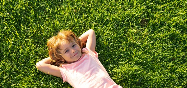 Banner with spring child face. Happy child lying on grass background. Cute kid child boy enjoying on field and dreaming. — Stockfoto