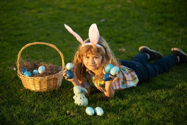 Mały króliczek z króliczymi uszami. dzieci chłopiec polowanie wielkanocne jaja w park układanie na trawie. — Zdjęcie stockowe