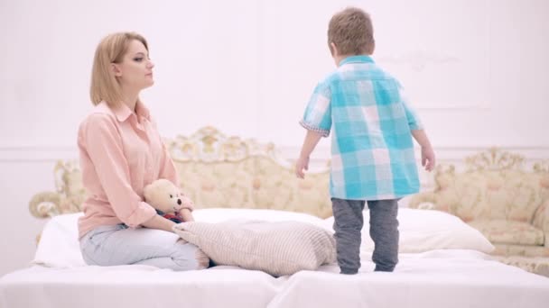 Mutter und Kind unterhalten sich im Schlafzimmer. Mutter und Sohn spielen im Bett. Mutterschaft und Elternschaft, glückliche Kindheit. — Stockvideo