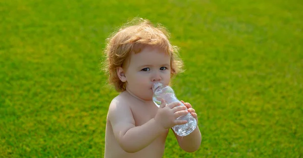 Child baby resting in grass park on nature, drinks clean water in summer grass park. — стоковое фото