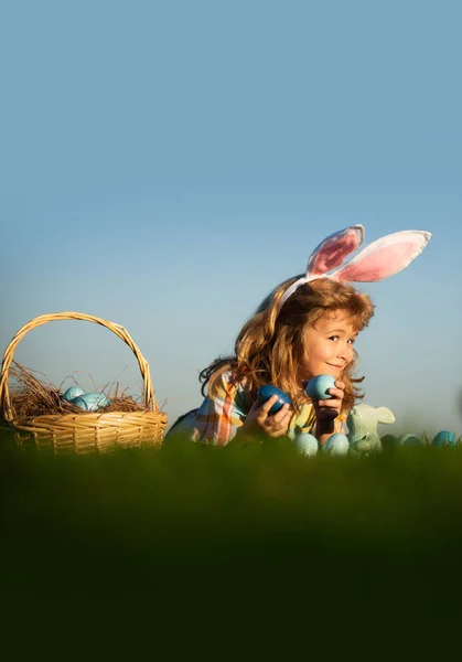 Dítě chlapec lov velikonoční vajíčka na jaře trávník kladení na trávě na obloze pozadí s kopií prostoru. — Stock fotografie