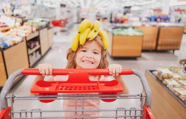 Child with shopping cart at grocery store or supermarket. Kid buying banana fruit in grocery market. — Stock Photo, Image