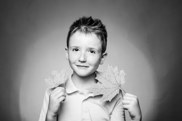 Rothaariger Junge, der mit Blättern spielt und in die Kamera blickt. Lifestylekonzept für die Kindheit. Herbstzeit für den Modeverkauf. Porträt aus nächster Nähe. — Stockfoto