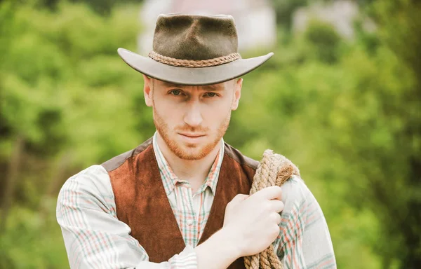 Guy cowboy. Owner of ranch. Farm worker and farming concept. Cowboy with lasso rope on green background. Handsome man in cowboy hat and rustic style outfit. — Stock Photo, Image