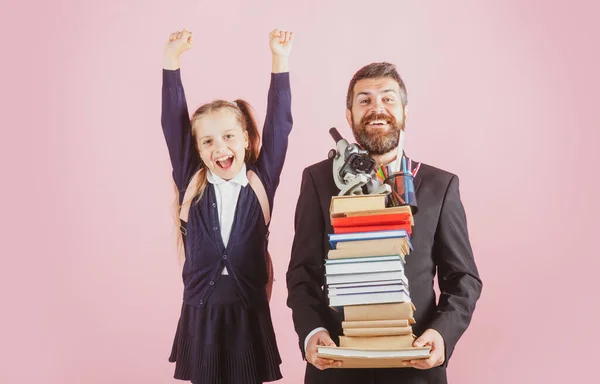 Πατέρας ή δάσκαλος κατέχουν μεγάλα βιβλία του σχολείου στοίβα σημειωματάρια. Ευτυχισμένος ενθουσιασμένος preteen κορίτσι φοράει σχολική στολή κρατώντας σακίδιο απομονώνονται σε ροζ, πορτρέτο. — Φωτογραφία Αρχείου