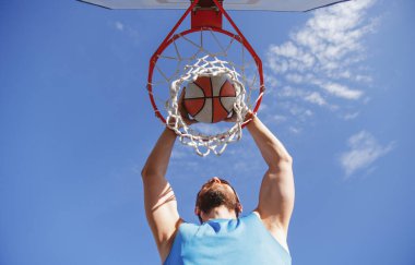 Young basketball player dunking basketball on outdoor court.