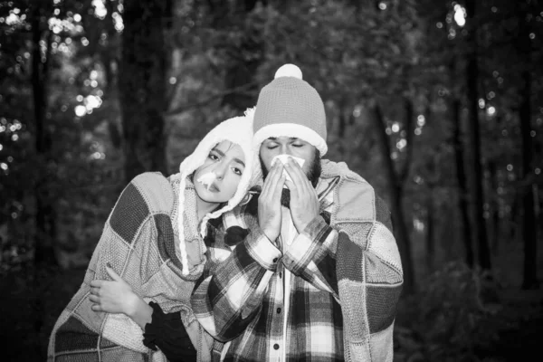 Pessoas espirrando em lenço outono ao ar livre. As pessoas têm gripe, têm corrimento nasal. Um jovem casal durante o tratamento da doença no fundo do parque de outono. Temporada da gripe, vacinação . — Fotografia de Stock