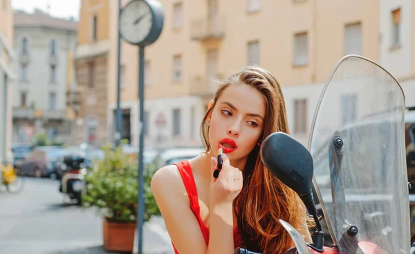 Sexig tjej med röda läppar sätta läppstift tittar i en spegel av motorcykel. Gatumodell. Stadsliv. — Stockfoto