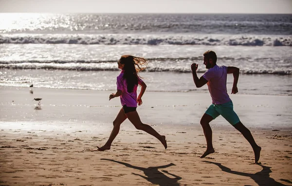 Sport und gesunder Lebensstil, Freunde joggen bei Sonnenuntergang am Strand. Silhouette Paar läuft am Strand. — Stockfoto