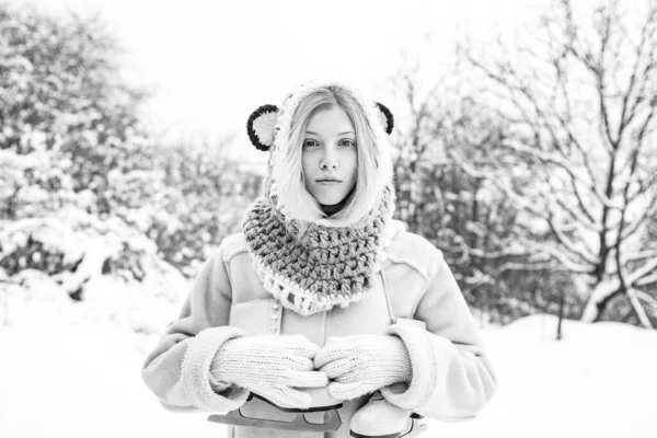 Νεαρή ξανθιά γυναίκα με πουλόβερ και αστείο καπέλο κρατώντας λευκά πατίνια πάνω από τον ώμο σε παγωνιά χειμερινής μέρας. Χειμερινές διακοπές. Κορίτσι που παίζει με το χιόνι στο πάρκο. — Φωτογραφία Αρχείου