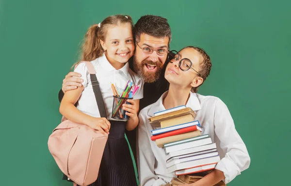 Retrato do pai e da escola crianças filhas abraçando no fundo quadro negro. A ler livros e a escrever. Pai ensinando meninas da escola em sala de aula. — Fotografia de Stock