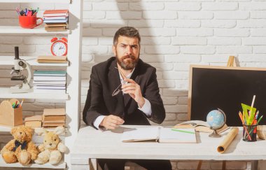 Portrait of teacher from preschool or elementary school in classroom. Handsome bearded tutor man near blackboard.