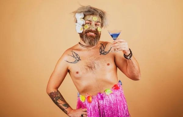 Funny man in hawaii. Male model with clay mask and cucumber slices on face. Man having cosmetic moisturizing mask hawaiian flowers drink cocktail, isolated studio background. Male face care. — Stock Photo, Image